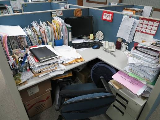 正在處理的相關文件堆滿了桌面，還有許多文件以開放式紙箱存放在桌子底下，已經影響到人員坐的姿式